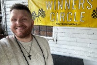Joey Carlsen Martinez stands smiling in front of a banner that says "Winners Circle"