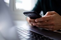 A pair of hands holds a smartphone above a laptop keyboard