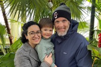 Family photo of a man in his 40s with wife and young son smiling in a tropical location.