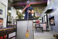 Man in the process of blowing glass at end of a long tube.