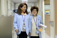 Two women wearing blue MSK volunteer jackets walk smiling down a hospital hallway.