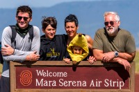 Family of five posing in the sun behind sign for air strip in Kenya smiling for camera.