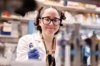 Young female scientist smiling in white coat and holding pipette. 