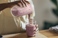 A pink smoothie is poured from a pitcher into a glass