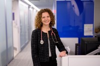 Dr. Zsofia Stadler smiles while leaning on a desk and wearing a stethoscope around her neck