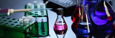 Test tubes and glass vials and beakers sit on a desk in a laboratory.