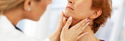 Female doctor examining woman’s thyroid area (throat).