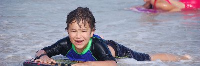 Smiling boy lying on board in the surf at the beach.