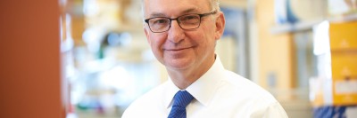 Head shot of doctor with glasses, white shirt, and blue tie in his lab.