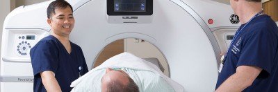 Two health care providers standing over a patient on a CT bed