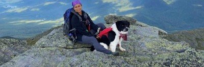 Elaine sitting down on a mountain with her border collie between her legs