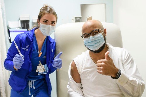 Мужчина показывает жест «палец вверх» рядом с медсестрой после вакцинации против COVID-19