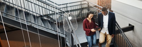 Young female and male coworkers walking downstairs looking at iPad