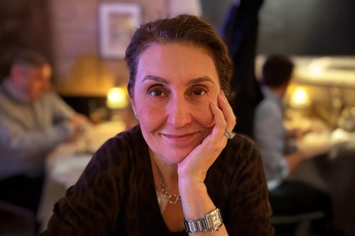 An MSK patient and advocate for people working with cancer, Gina Jacobson looks relaxed and smiles at the camera, with her left hand under her chin. 