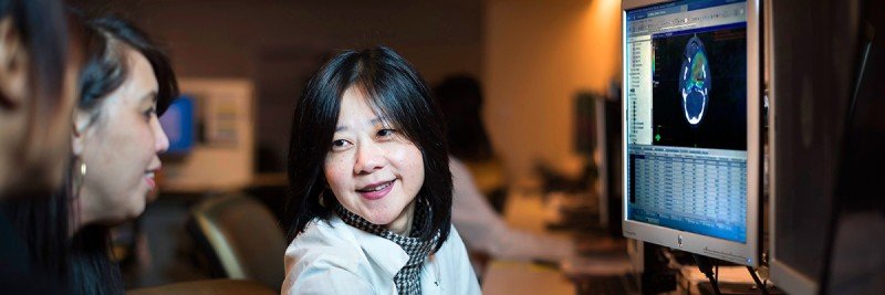 Female physician in white coat sitting at screen that shows medical image.